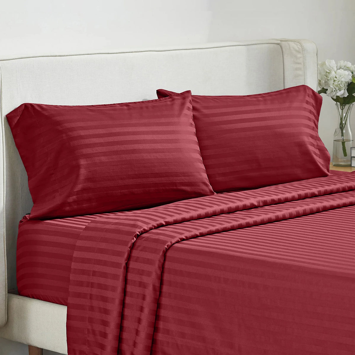 A set of luxury solid red striped bedding, including pillows and a fitted sheet, on a white upholstered bed.
