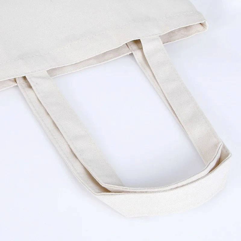 A light beige reusable canvas tote bag with fabric handles shown from the side.