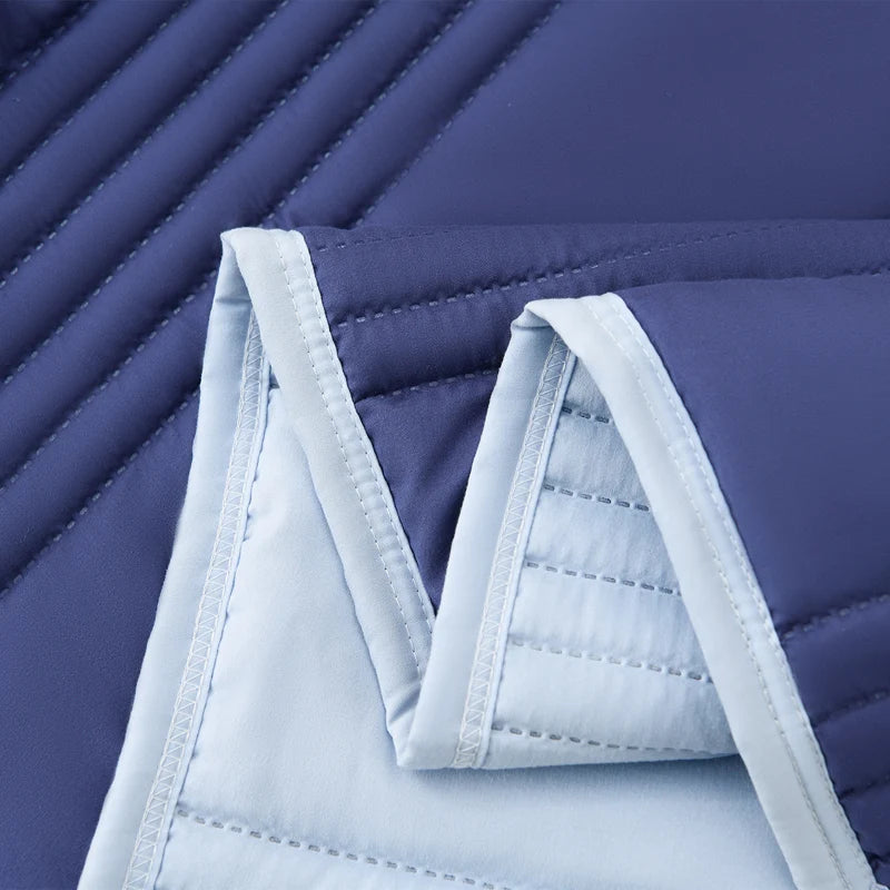 A close-up of a light blue quilted blanket folded on a dark purple surface.