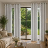 Four white linen textured blackout curtains hanging in a glass door frame with greenery visible outside