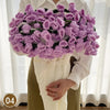 A hand knitted floral rose bouquet in purple and green shades held by a person.