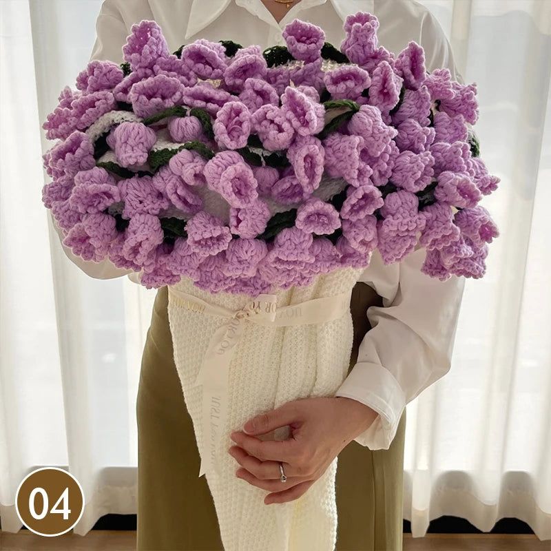A hand knitted floral rose bouquet in purple and green shades held by a person.