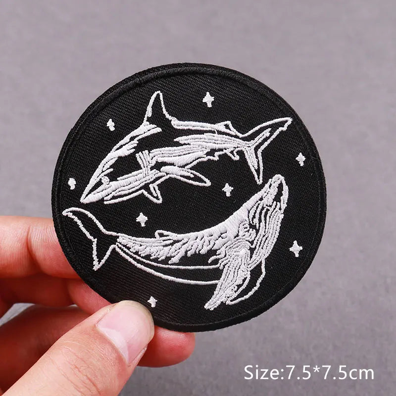 Black embroidered patch featuring a white silhouette of a shark and a whale swimming under stars