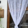 A sheer white floral lace curtain panel draped over a glass door.