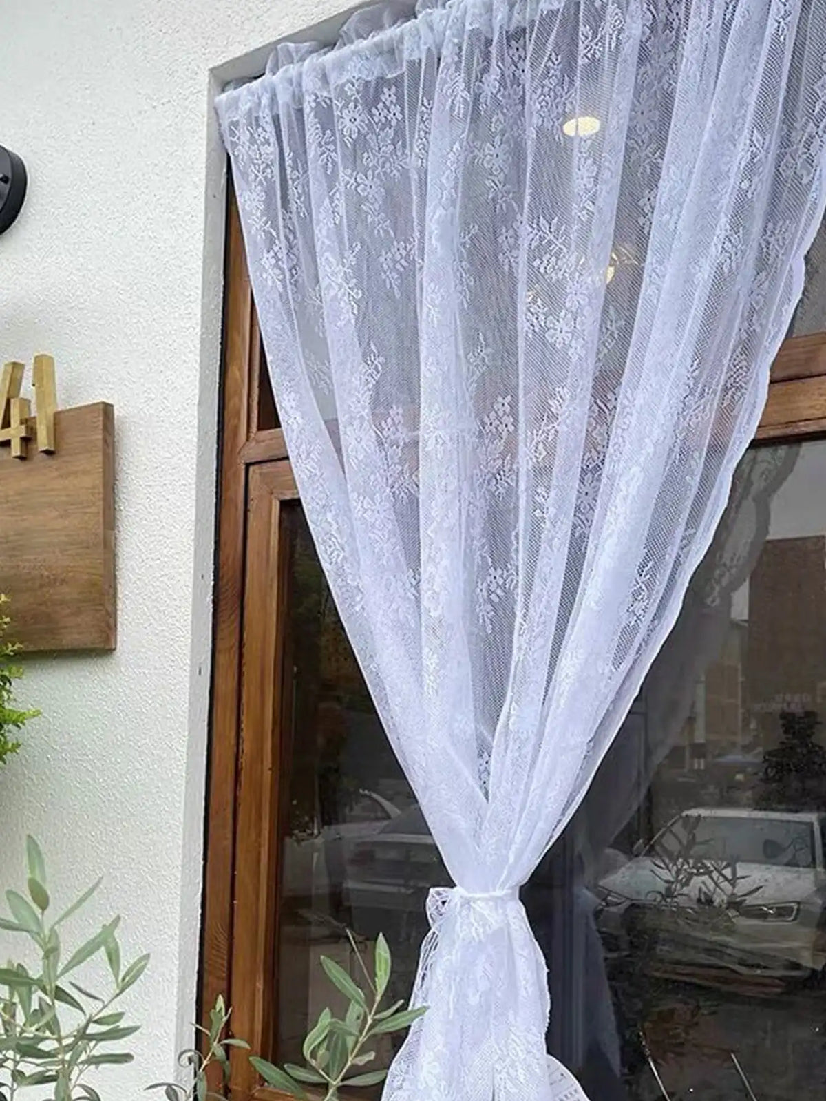 A sheer white floral lace curtain panel draped over a glass door.