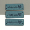 Three rectangular teal leather tags, each engraved with the words Made with and a heart design.