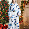 A woman models a white sherpa fleece oversized blanket hoodie with blue and purple penguin designs in a festive holiday setti