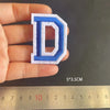 A hand holds a blue alphabet embroidery iron-on patch shaped like the letter D, measured against a ruler.