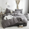 A gray duvet cover set with pom-pom decoration is displayed on a bed in a bright room.