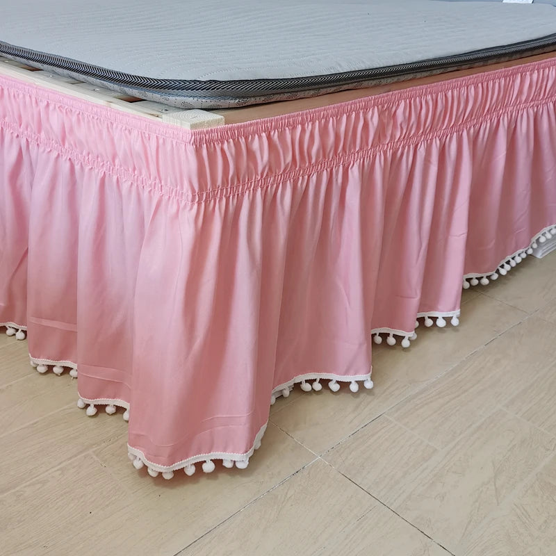 A pink elastic bed skirt with white trim is displayed on a wooden surface.
