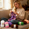 A woman is shown knitting or crocheting with various colored soft bulky chenille yarn on a couch.
