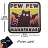 A black woven label embroidered with the text PEW PEW and MADAFAKAS featuring a cat silhouette against a yellow sun backgroun