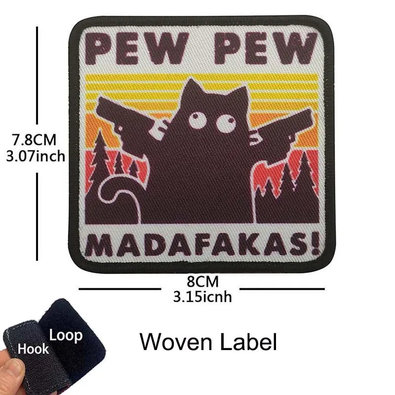 A black woven label embroidered with the text PEW PEW and MADAFAKAS featuring a cat silhouette against a yellow sun backgroun