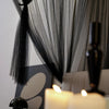 Elegant mosquito net bed canopy with sheer black fabric and warm candlelight.