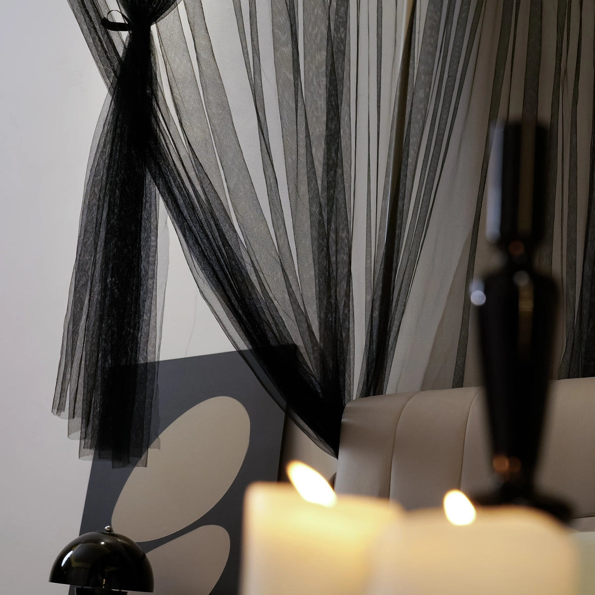 Elegant mosquito net bed canopy with sheer black fabric and warm candlelight.