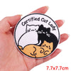 A hand holds a circular embroidered patch featuring cartoon cats, including a black cat and a white cat.