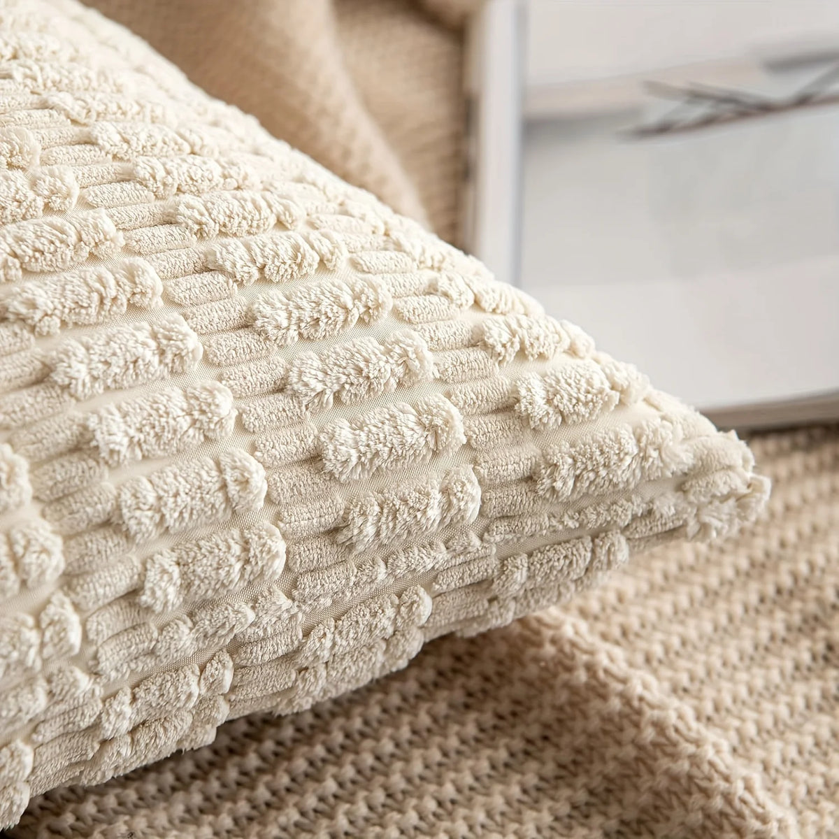 A cream-colored knitted throw pillow cover with a textured, repeating stripe pattern resting on a beige woven fabric.