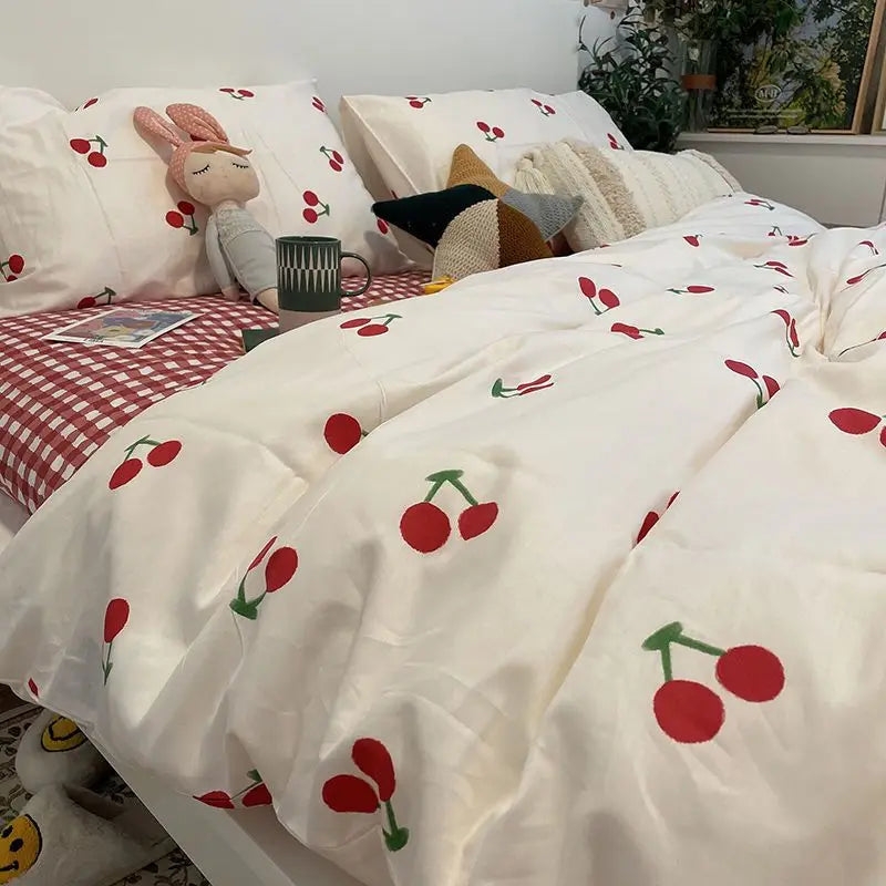 White bedding set with red cherry floral pattern and decorative pillows.