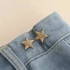 A close-up of a denim jean cuff featuring an adjustable metal star brooch pin.