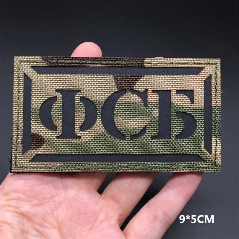 A rectangular tactical patch featuring the Cyrillic letters ПСС in a dark olive green fabric on a hand.