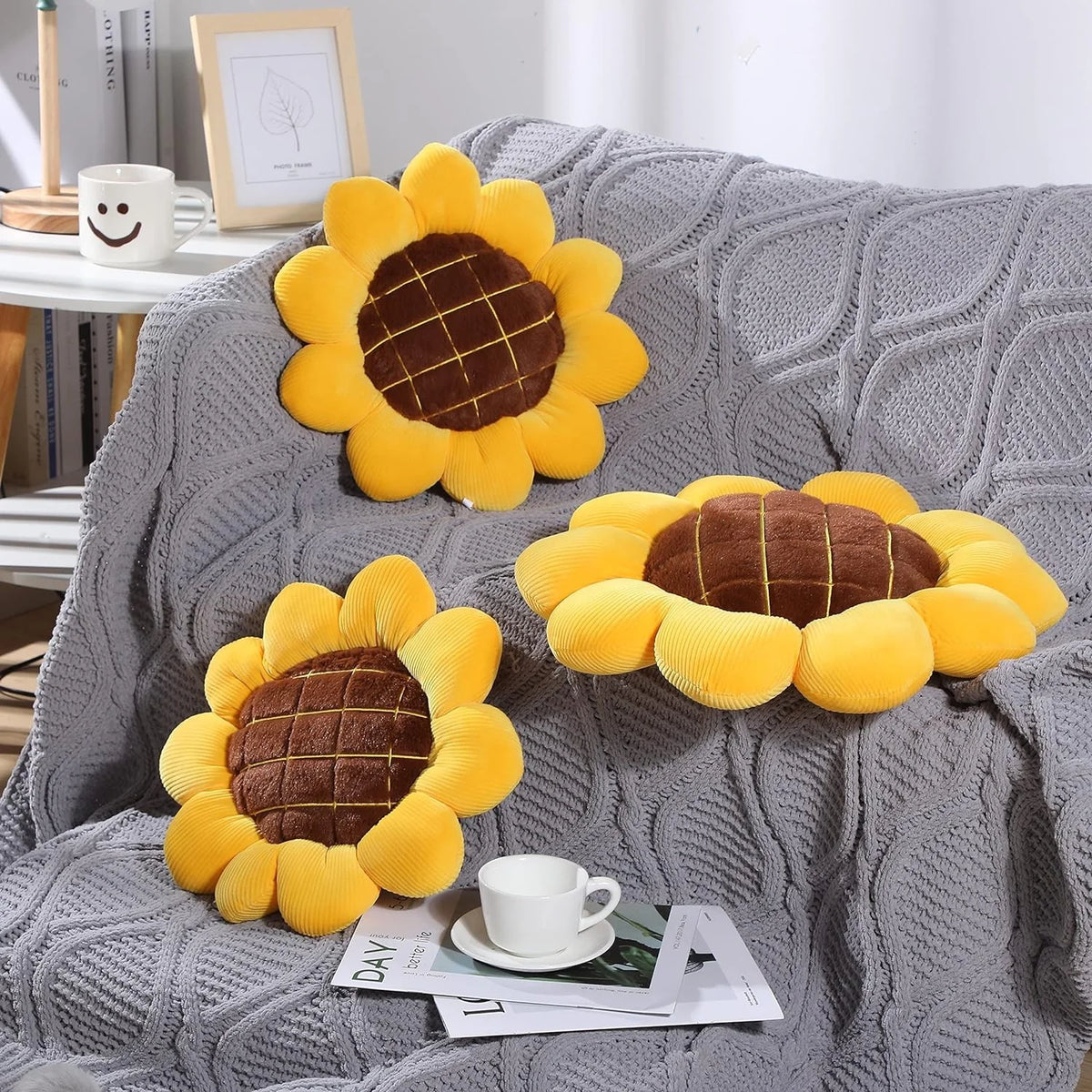 A yellow and brown sunflower shaped throw pillow resting on a gray knitted blanket.