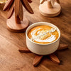 A ceramic bowl filled with orange-colored soup or puree is placed on a wooden placemat.