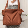 A brown foldable tote bag is shown being carried by a person wearing a white top and a checkered skirt.