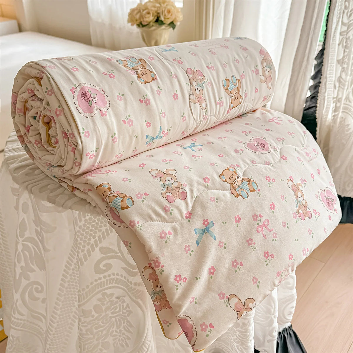A light pink and cream quilted blanket featuring a pastoral print of small animals like rabbits and flowers.