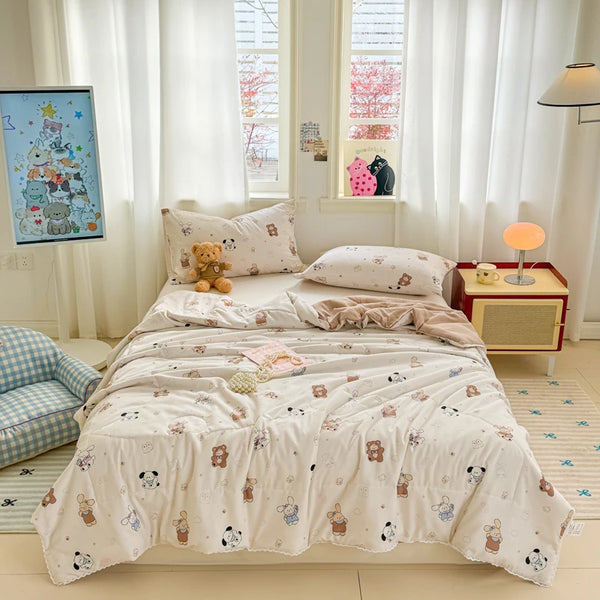 A light pink quilted blanket with small animal patterns is displayed on a bed in a bright room.