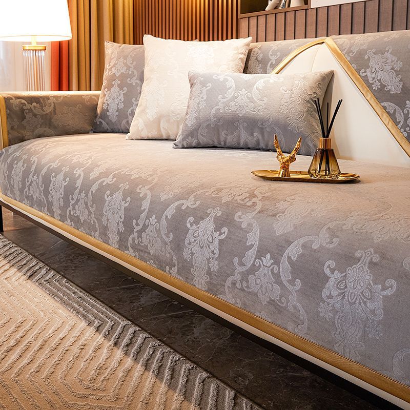A luxury velvet sofa cover featuring gray patterned fabric and cream pillows on a modern sofa.