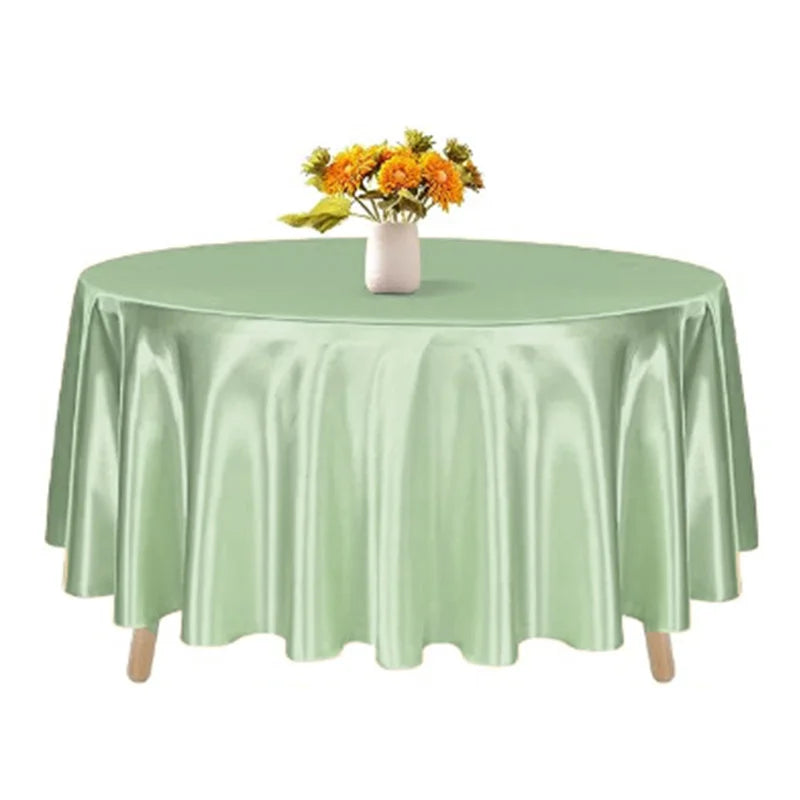 A satin green round table cloth set for elegant decor with a vase of yellow flowers.