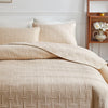 A beige quilted cotton bedspread set featuring a textured pattern and matching pillows on a bed.