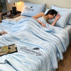 A woman rests on a bed covered with a light blue Dreamcity quilt, featuring a feather design.