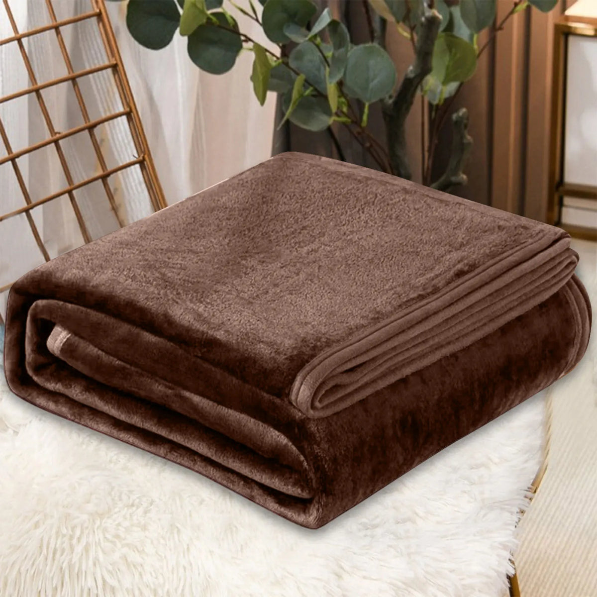 A dark brown cozy coral fleece throw blanket folded neatly on a white fluffy surface.