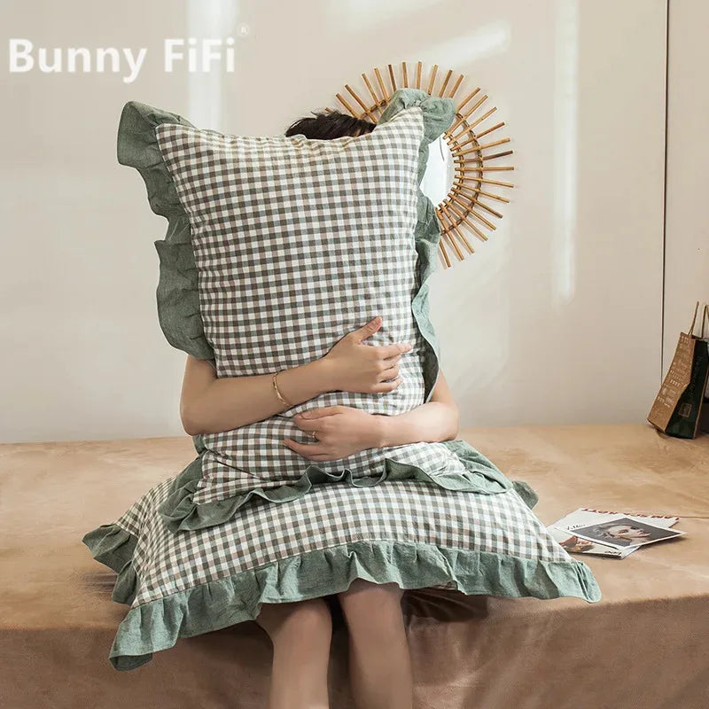 A person is holding a plaid washed cotton pillowcase with ruffled edges against a light background.