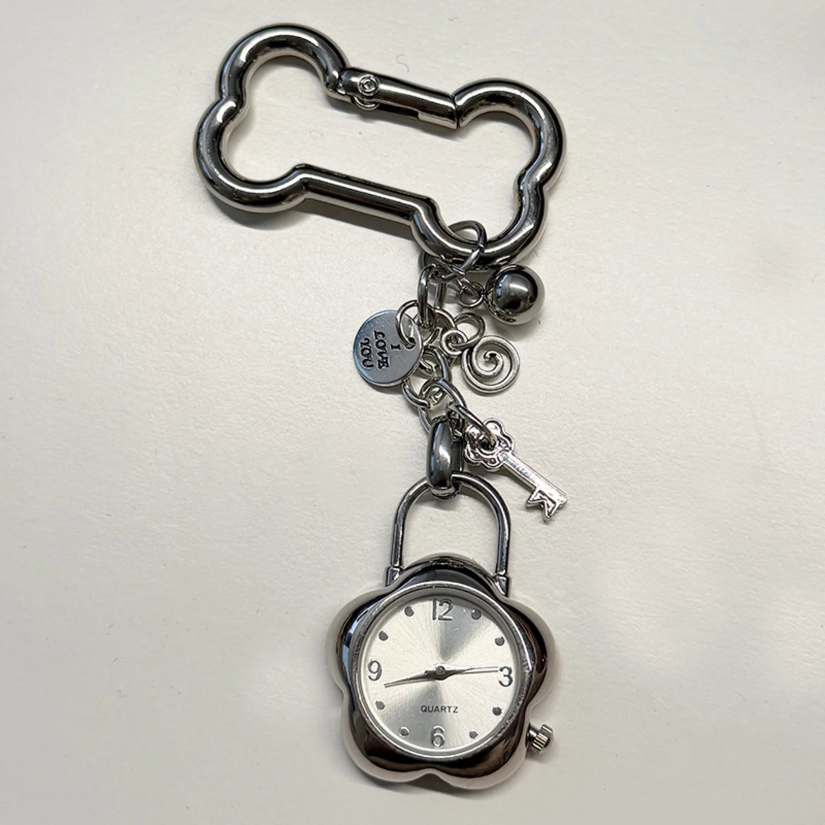 Silver pocket watch keychain featuring an adjustable clock mechanism and a key.