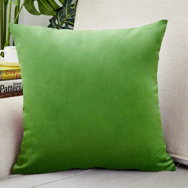 A square emerald green velvet cushion cover resting on a light-colored sofa.