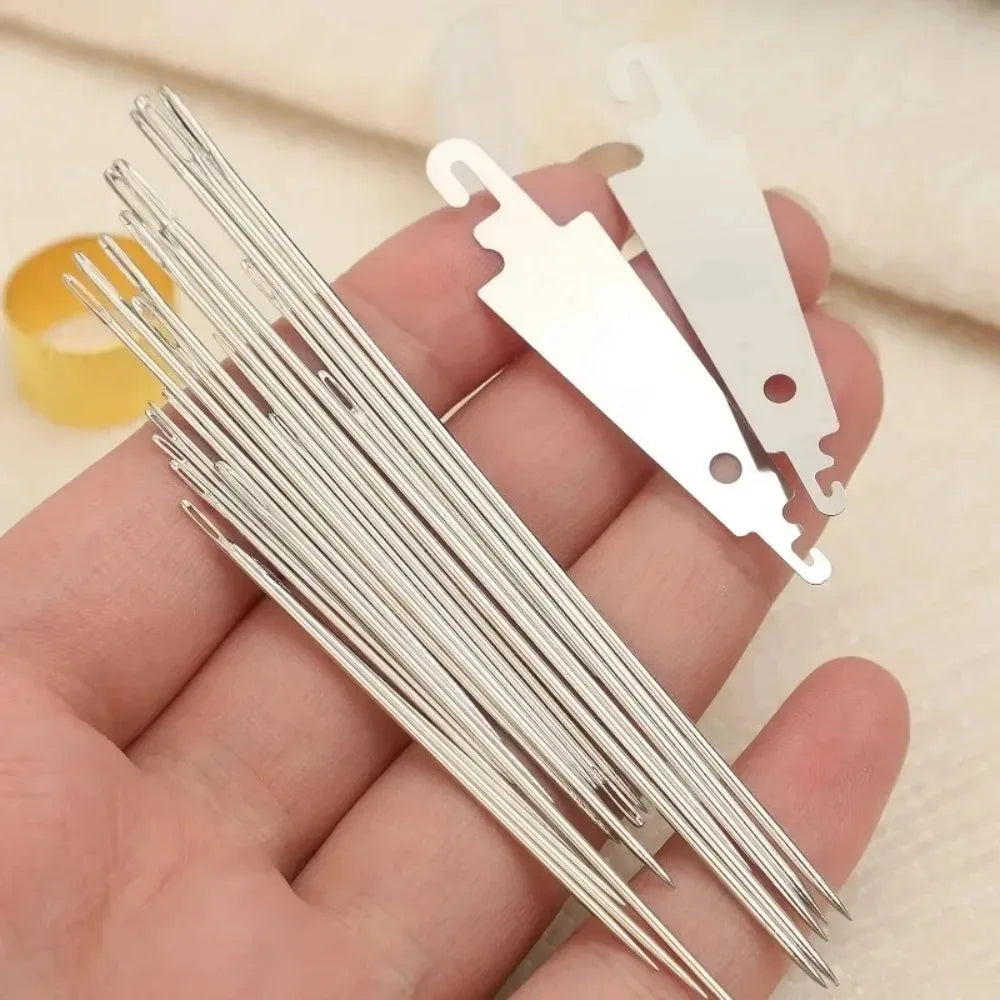 A hand holds a set of stainless steel big-eye sewing needles with their protective caps.