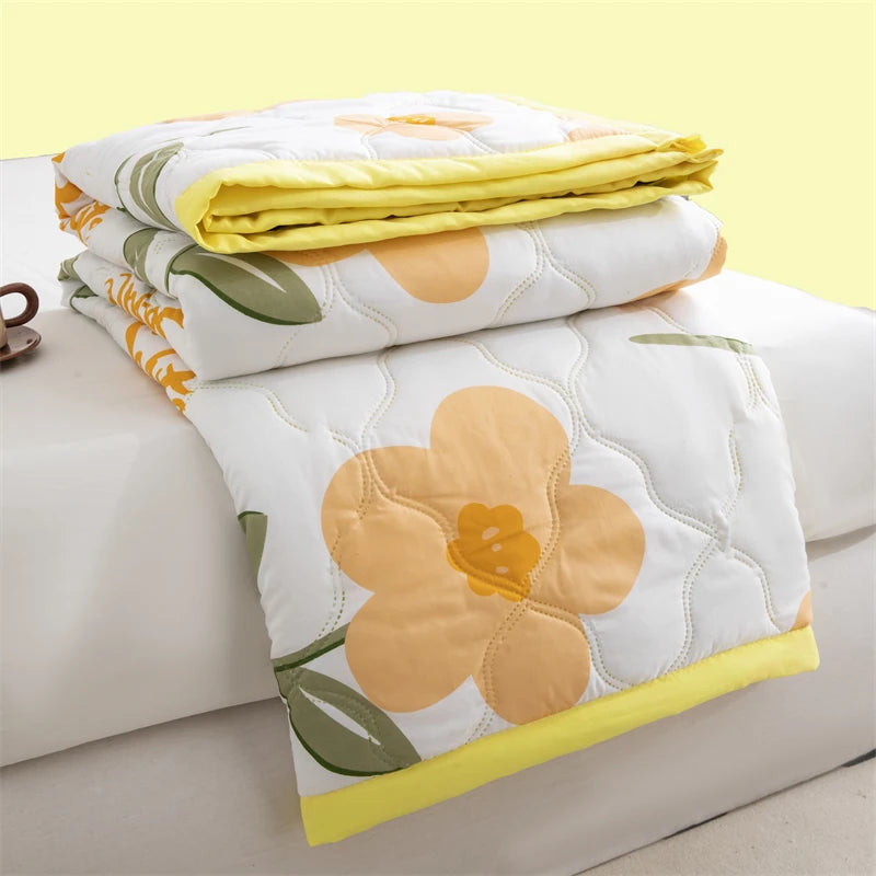 A stack of white floral patterned lightweight summer duvet covers and a folded yellow duvet.