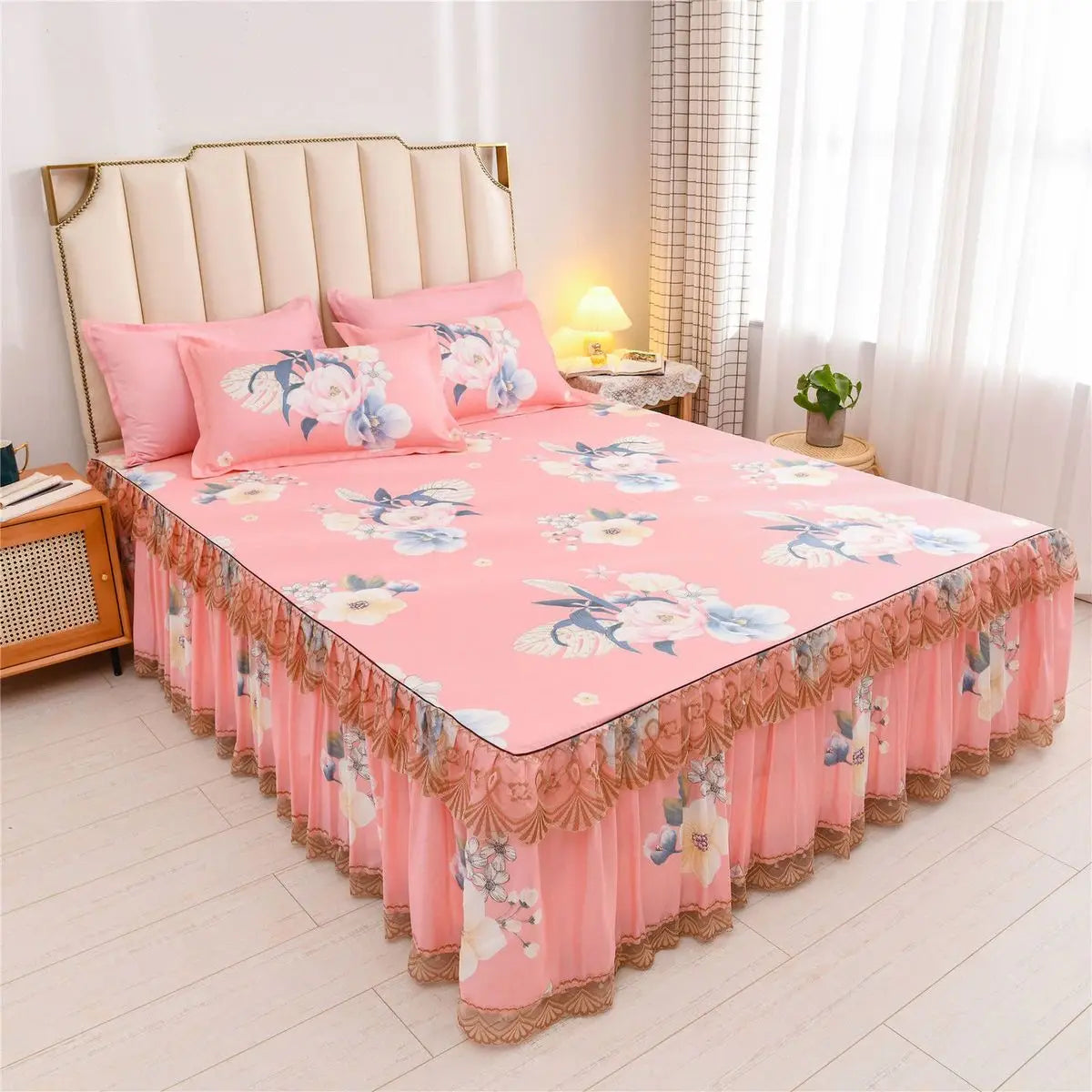 Pink floral bed skirt with ruffled hem protecting a mattress, set against a light-colored headboard and bedding.