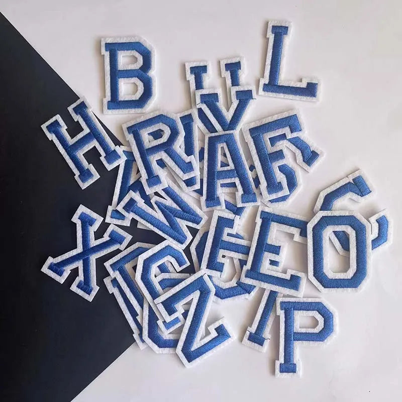 A collection of blue and white alphabet embroidery iron-on patches scattered on a dark surface.