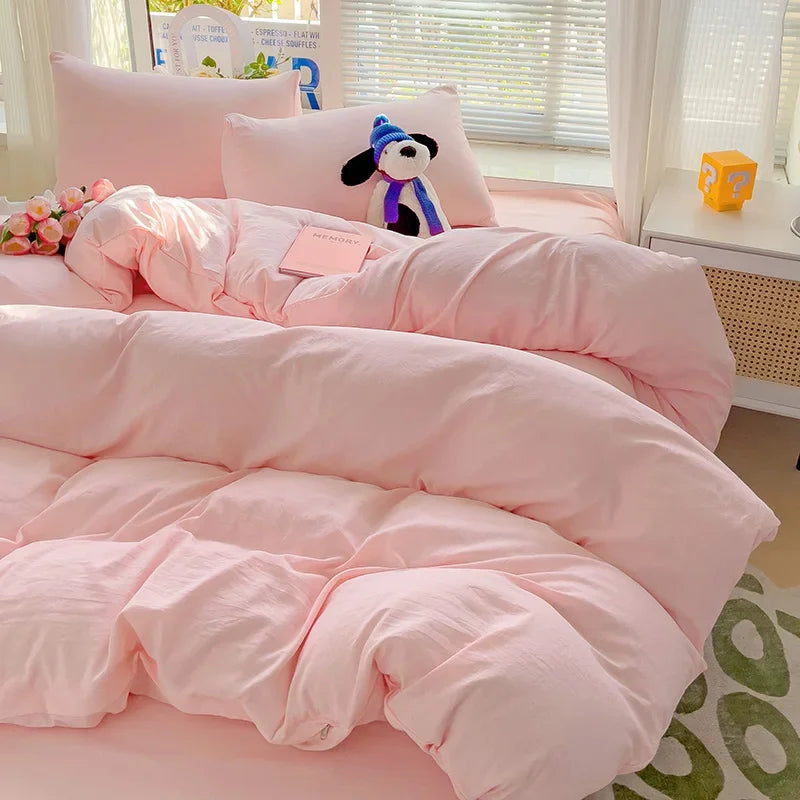 A pink solid cotton bed linen set with a duvet and pillows is displayed on a bed.