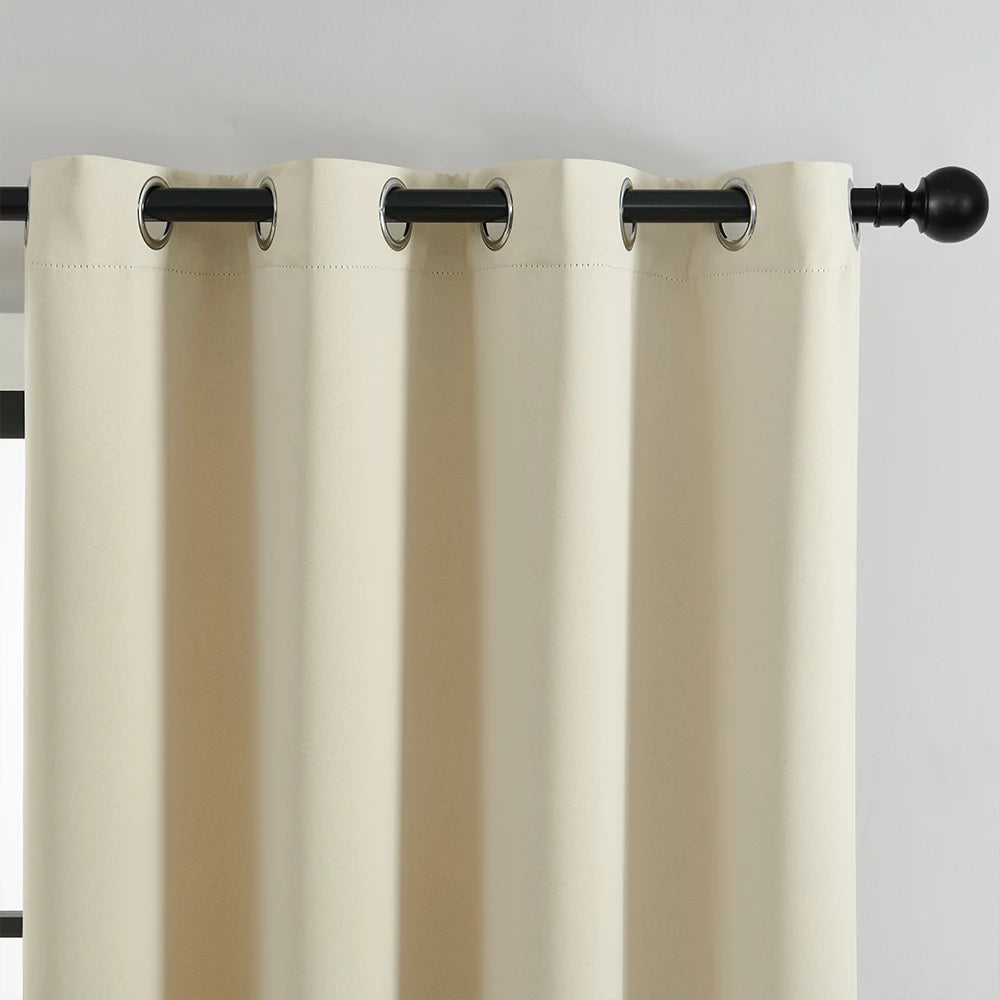 A floor-length, light beige blackout window curtain hanging from a black rod.
