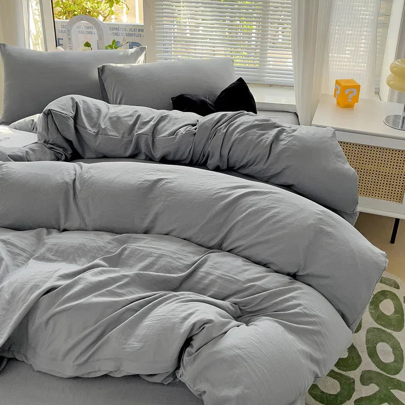A gray solid cotton bed linen set with a duvet and pillows is displayed on a bed.