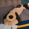 A giant soft cotton dog plush pillow doll with brown and tan fur resting on a gray bed.