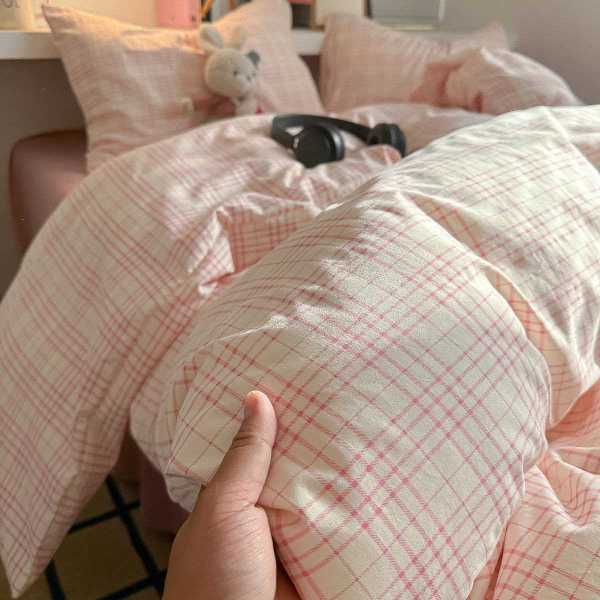 A close-up of a pink plaid duvet cover and pillow set with light pink accents on a bed.