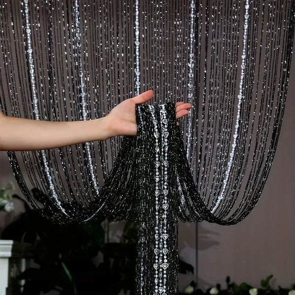 A hand is adjusting a black acrylic tassel beaded room divider curtain.