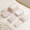 A set of cream-colored leather travel storage organizers and pouches arranged on a white bed with a knit blanket.