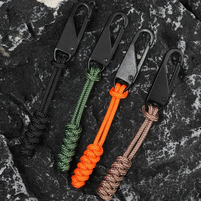 Four detachable zipper pull sliders in black, green, orange, and brown cord on a dark textured surface.