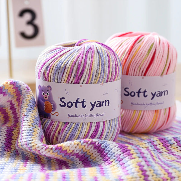 A ball of soft yarn in pink and multicolored stripes is displayed next to a knitted fabric swatch.